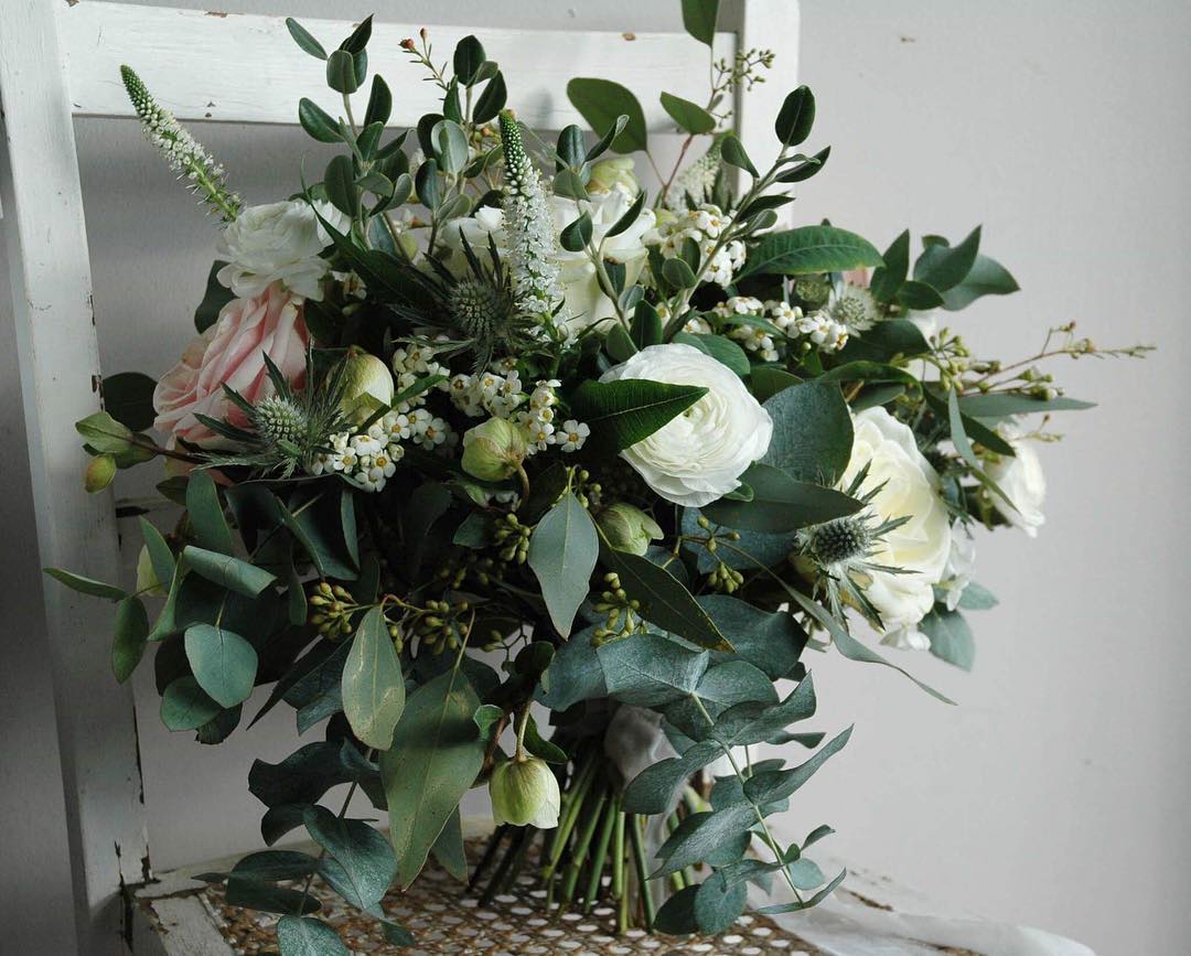 Bouquet of white and pink flowers with green foliage, resting on a white chair.