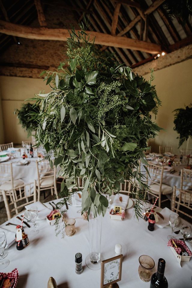 Wedding reception with a large green floral centerpiece on a round table, set in a rustic barn.
