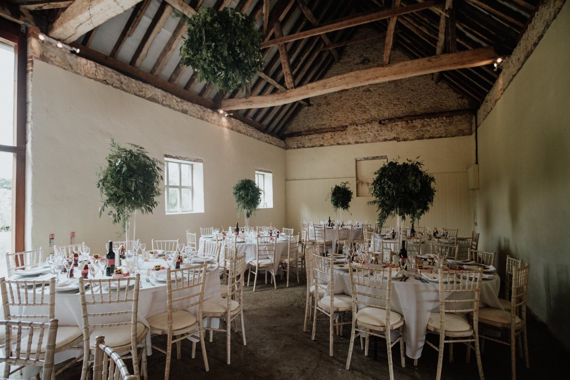 Wedding reception in a barn with round tables, white chairs, and floral decorations.