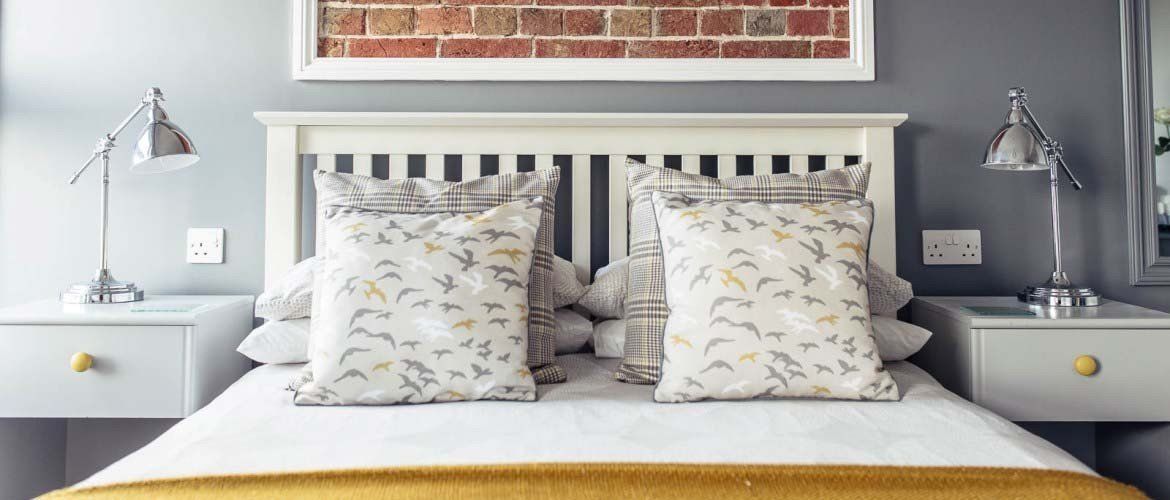 Bedroom with white bed frame, gray walls, bedside tables, lamps, and decorative pillows.