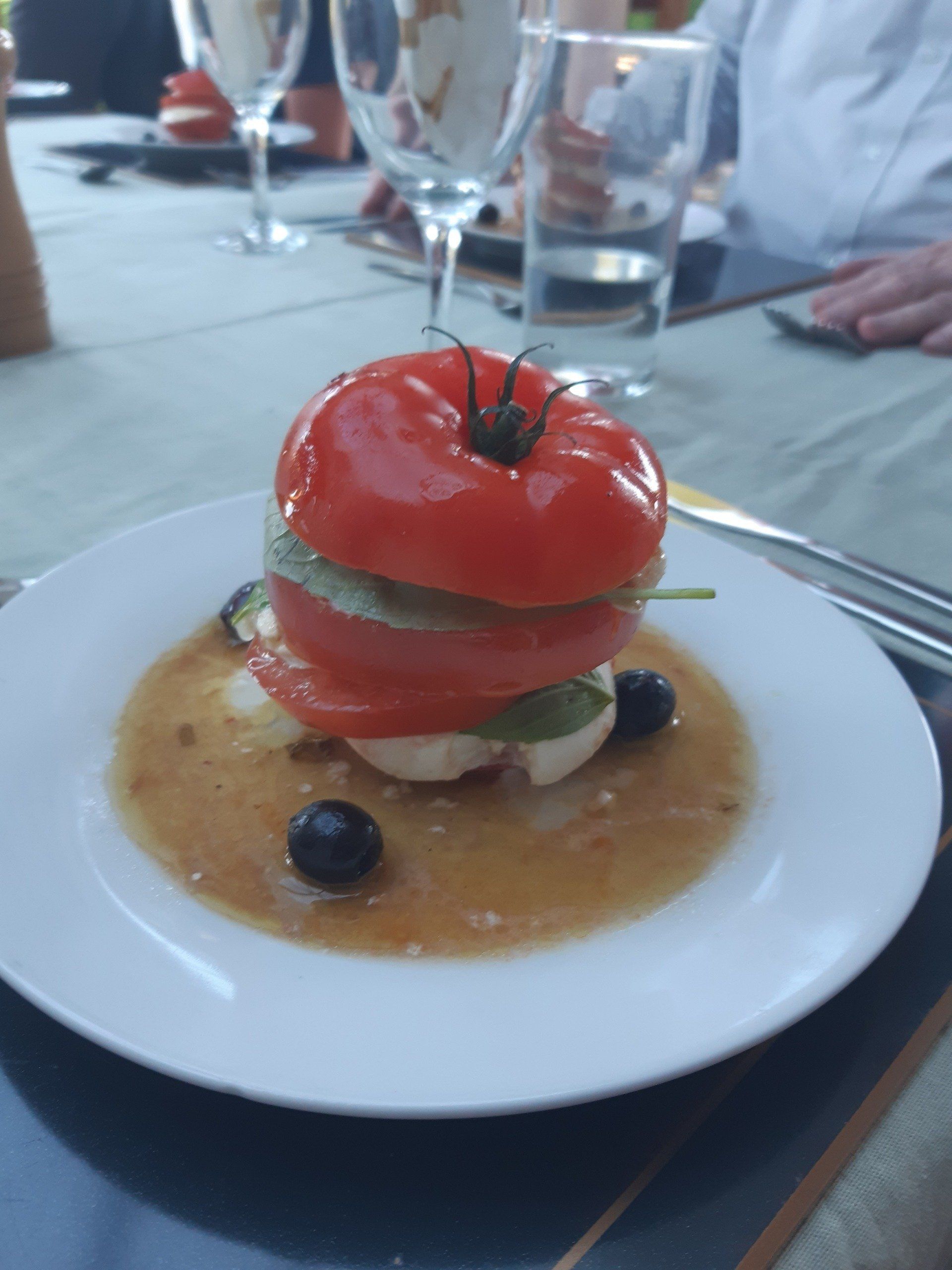 Stacked tomato and mozzarella salad with basil and olives, served in a sauce.