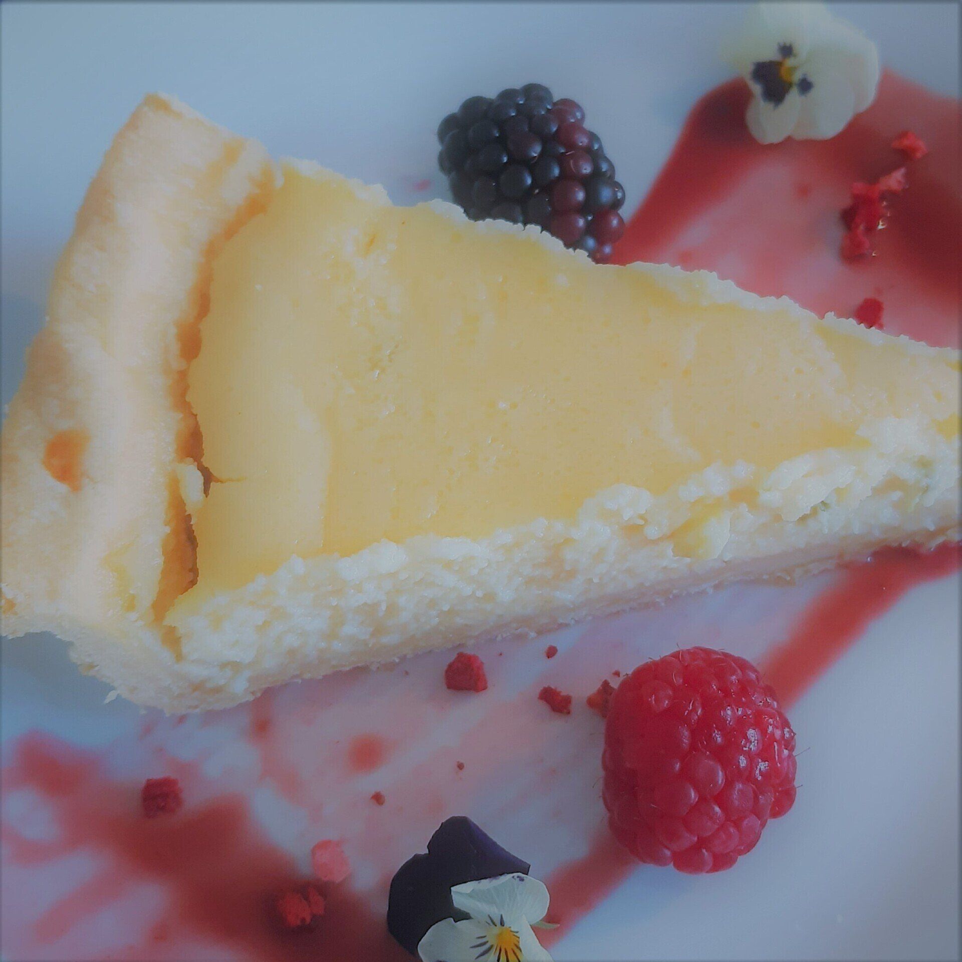 Slice of cheesecake with berries and sauce on a white plate.