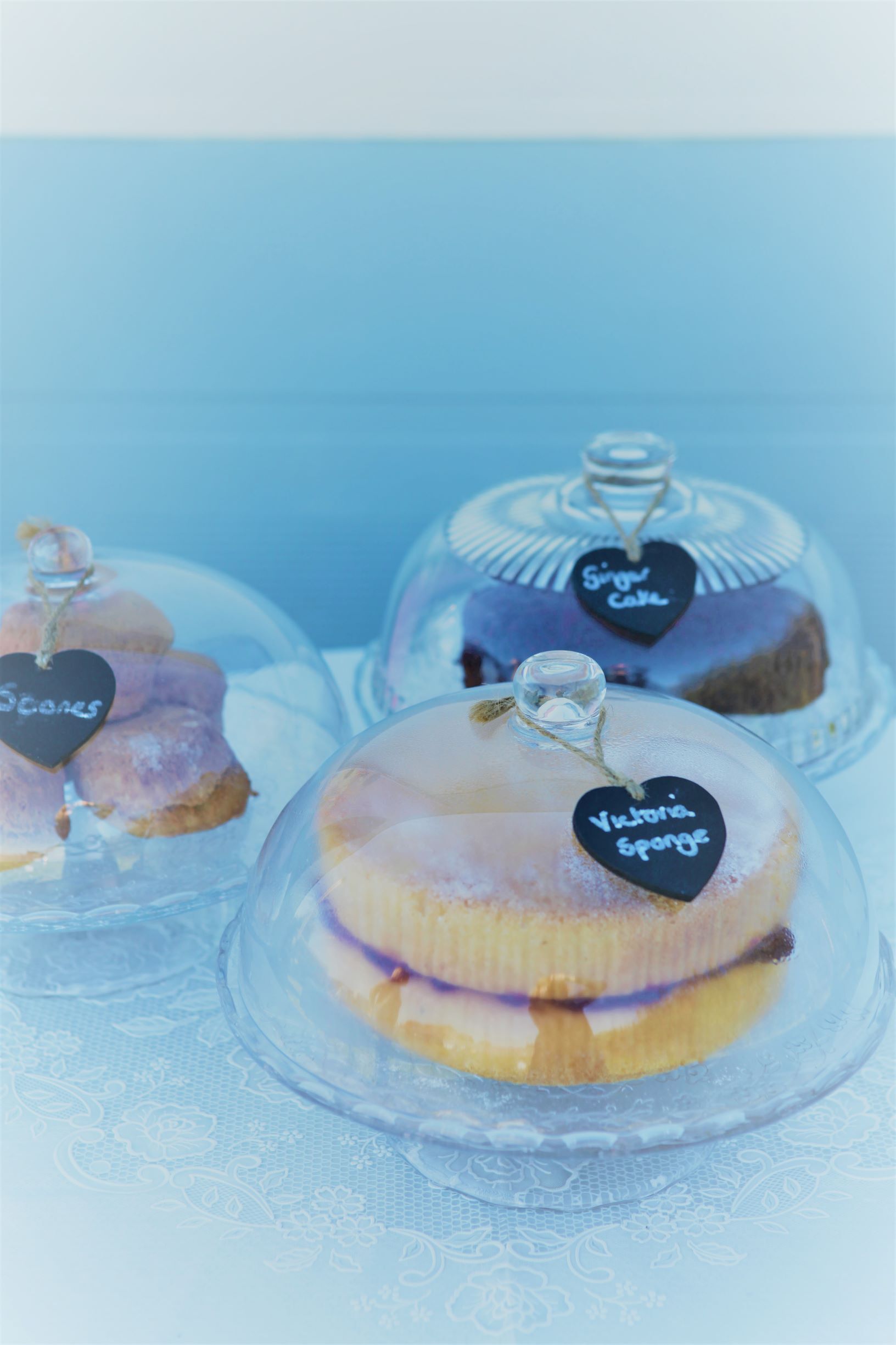 Cakes displayed under glass domes with heart-shaped chalkboard labels; on a white surface.