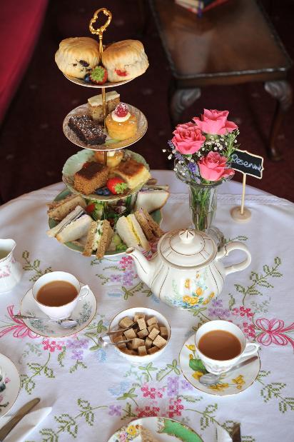 High tea table setting with tiered desserts, sandwiches, and tea cups.