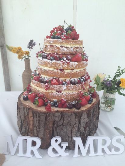 Naked wedding cake on a wooden base, decorated with berries and powdered sugar,