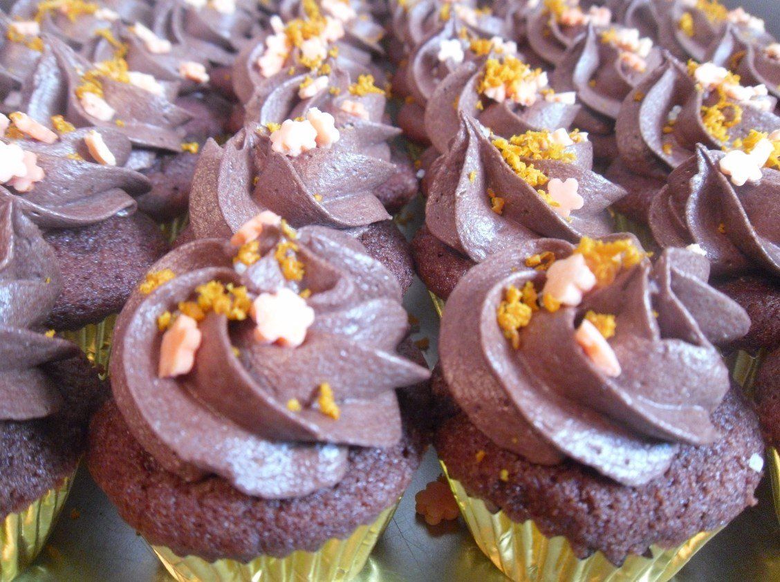 Chocolate cupcakes with swirled frosting, topped with orange and pink sprinkles, arranged closely together.