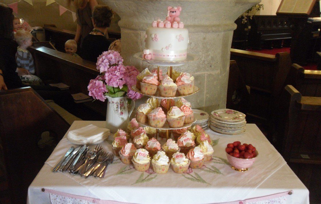 Cake and cupcakes on a table in a church setting, decorated in pink and white for a celebration.