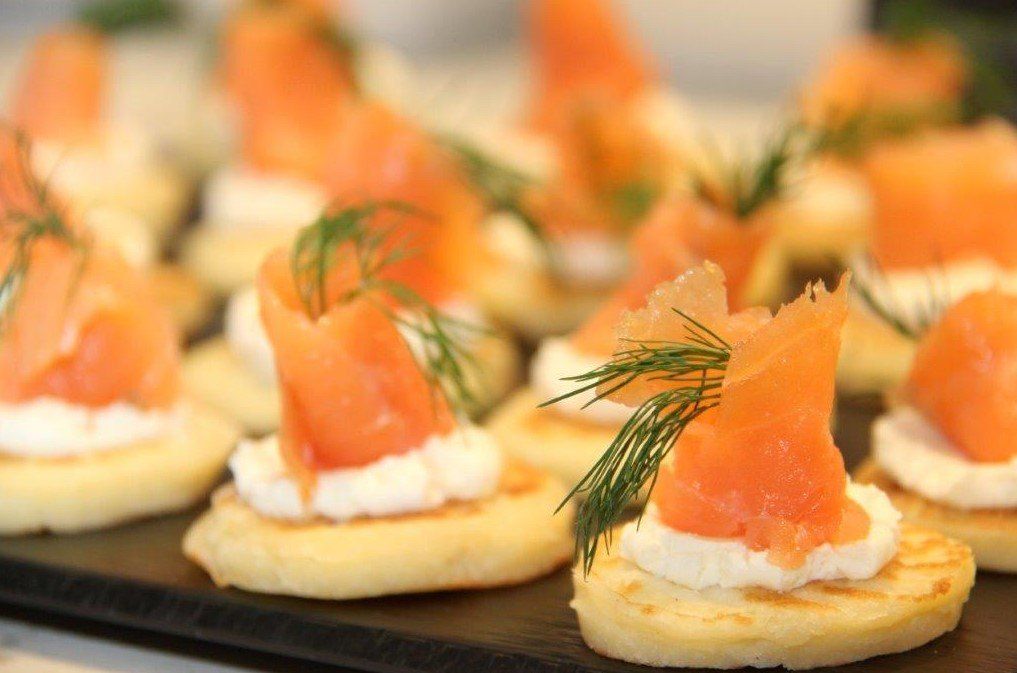 Smoked salmon canapés with cream cheese and dill on a black tray.