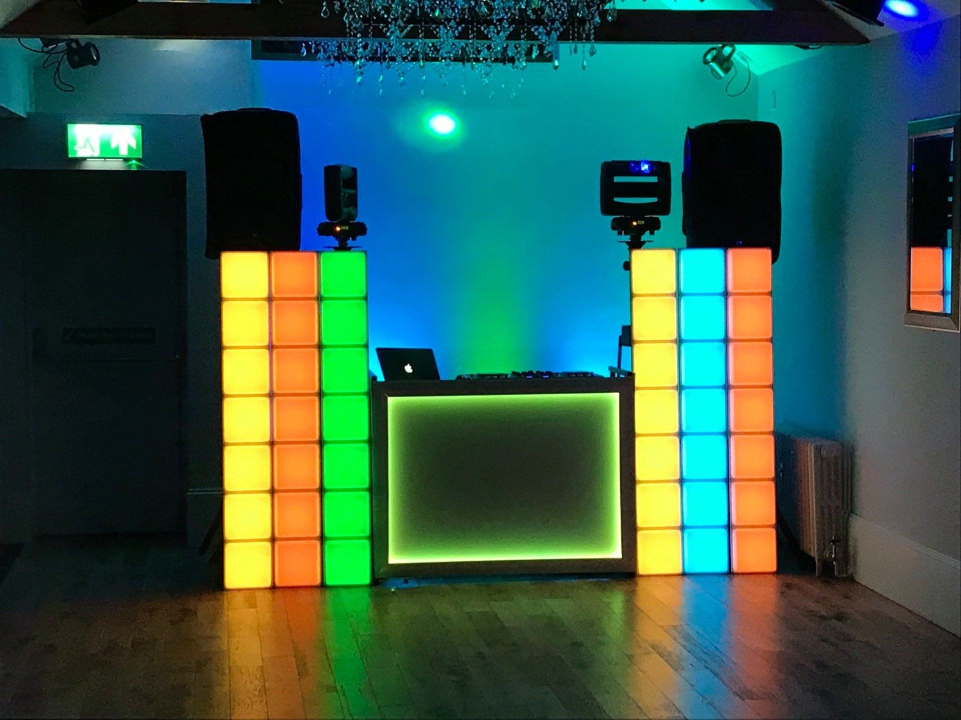 DJ setup with illuminated colored columns and a black DJ booth, in a room with speakers.
