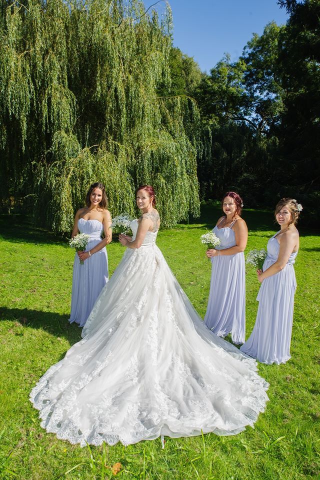 Bride in white gown with bridesmaids in light blue dresses posing on green grass.
