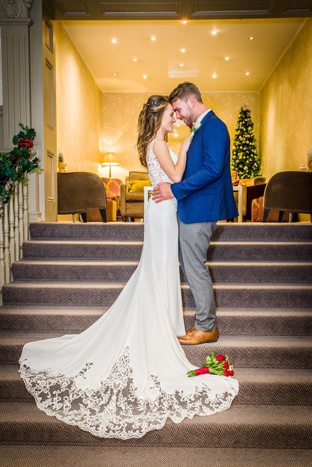Bride and groom embrace on stairs. The bride wears a white dress with a train, the groom wears a blue jacket.