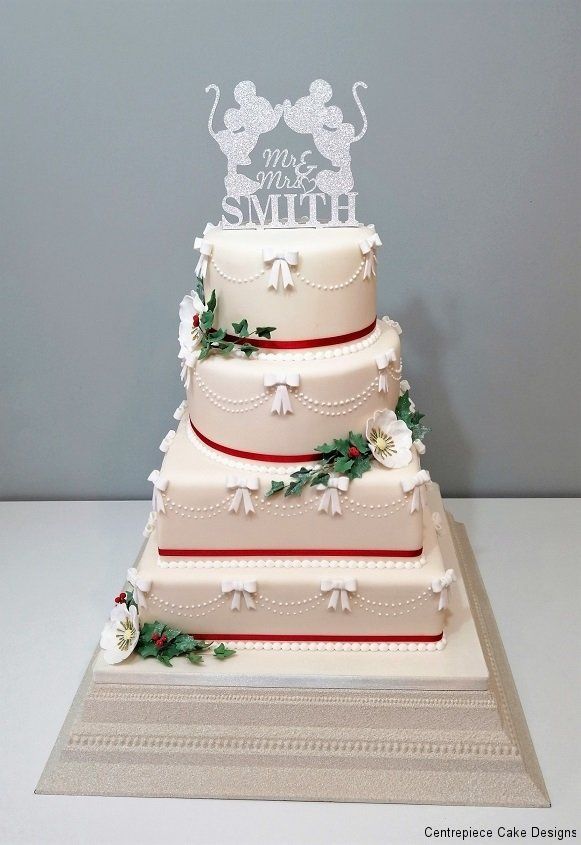 Four-tiered wedding cake with white frosting, red ribbons, bow details, and a Mickey Mouse topper.