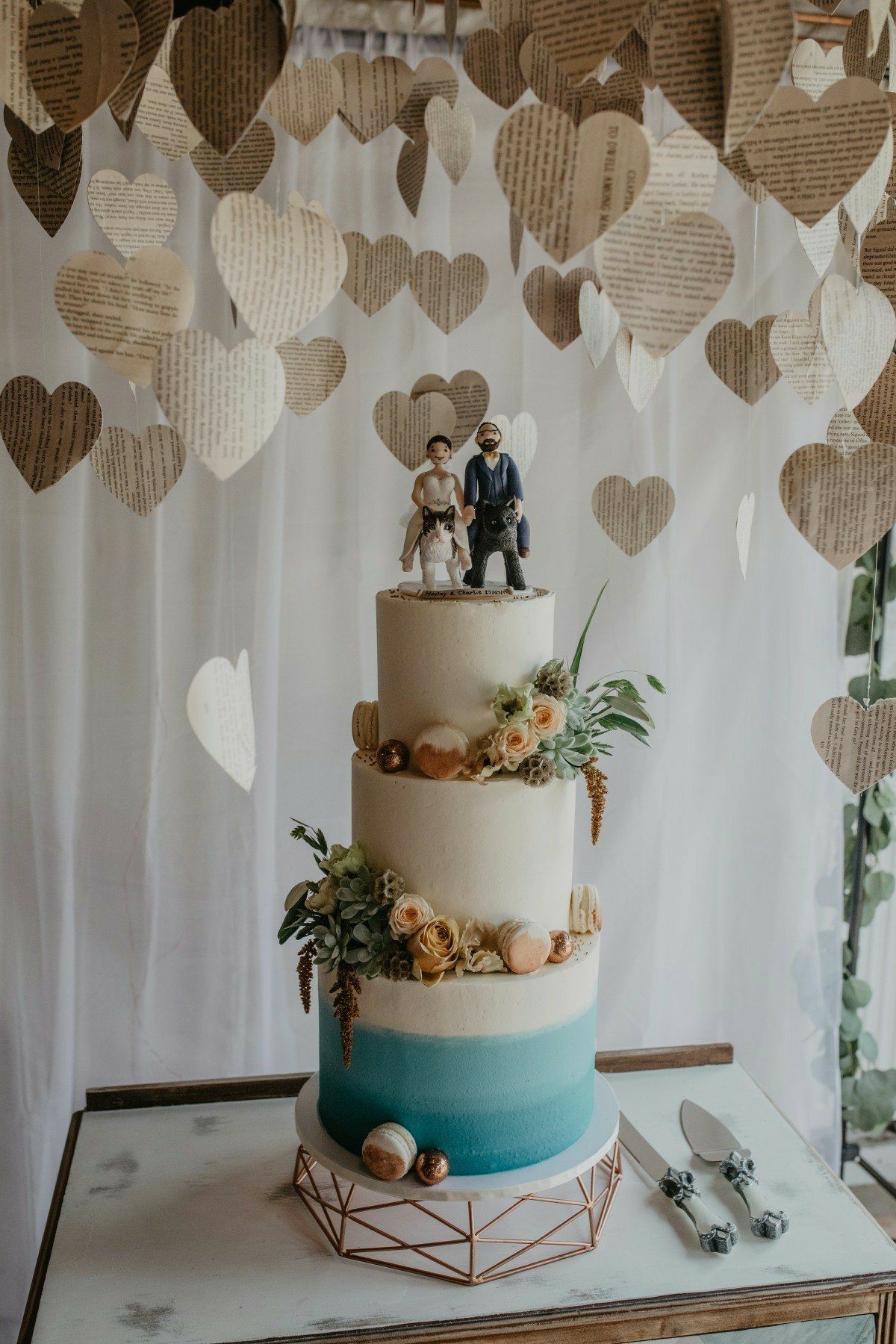 Three-tiered wedding cake with Star Wars figurines, decorated with flowers, sitting on a table, with heart decorations in the background.