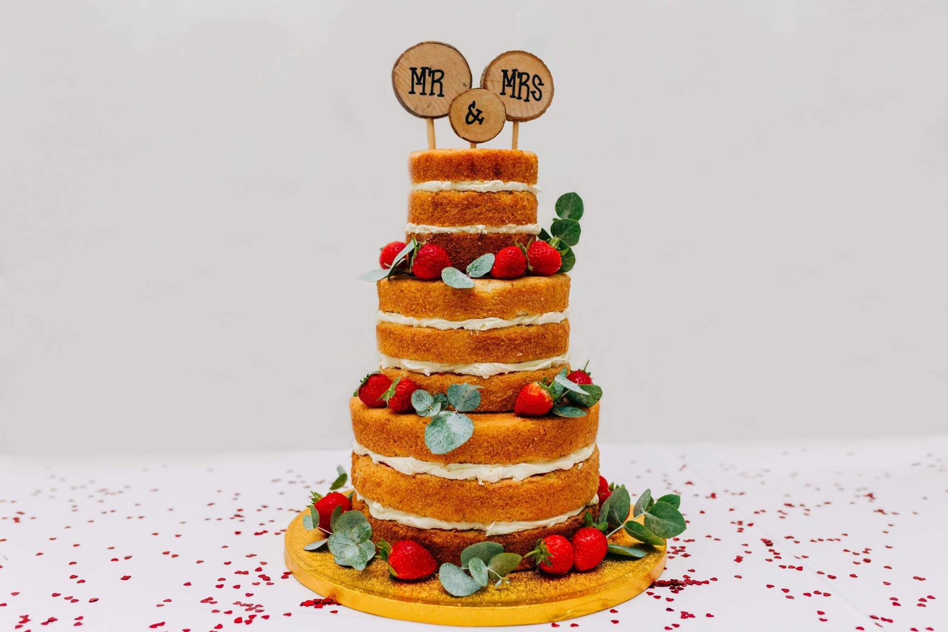 Naked-layer wedding cake with strawberries and greenery, topped with