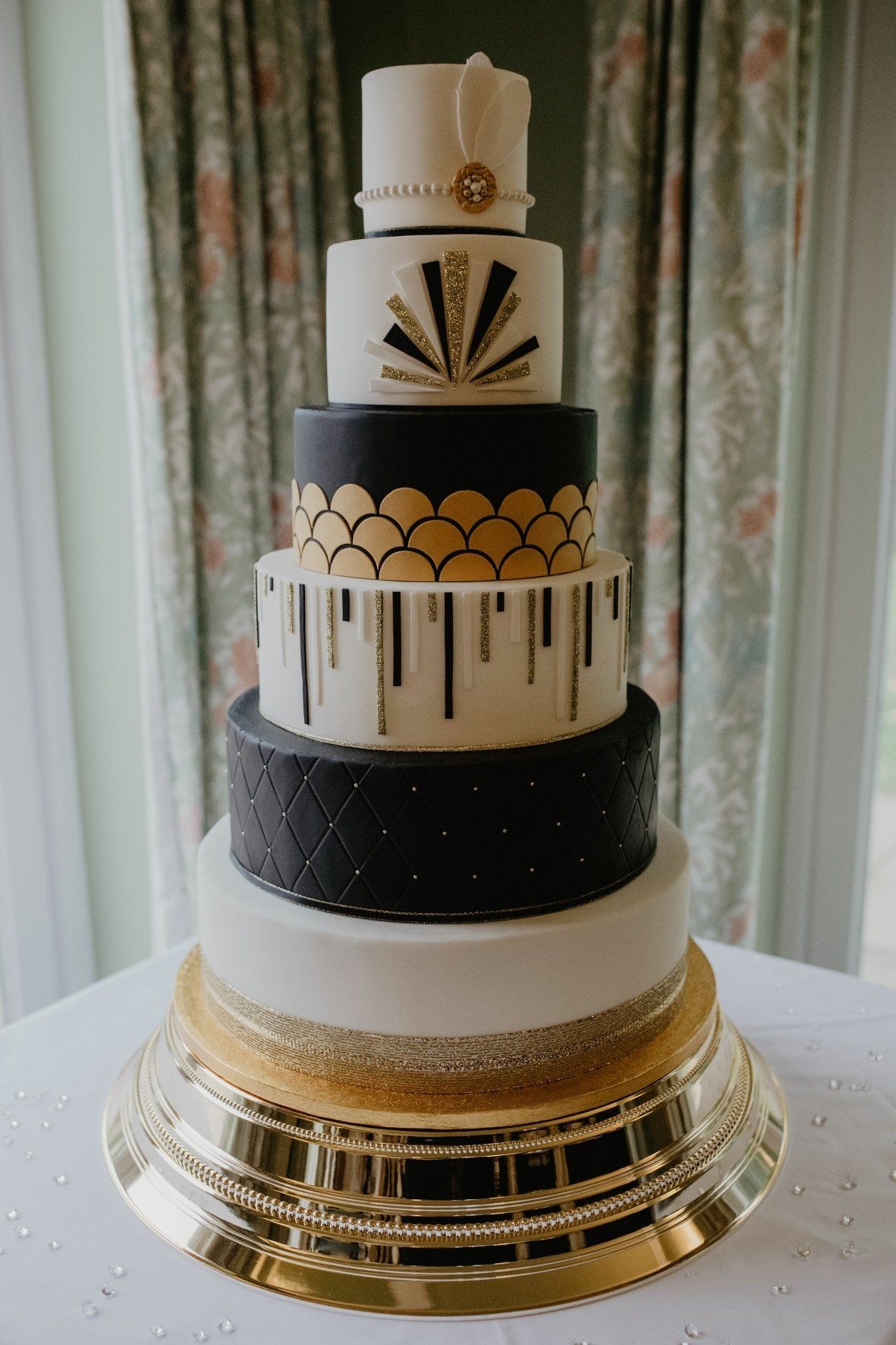 Six-tiered art deco cake with gold and black accents on a golden stand.