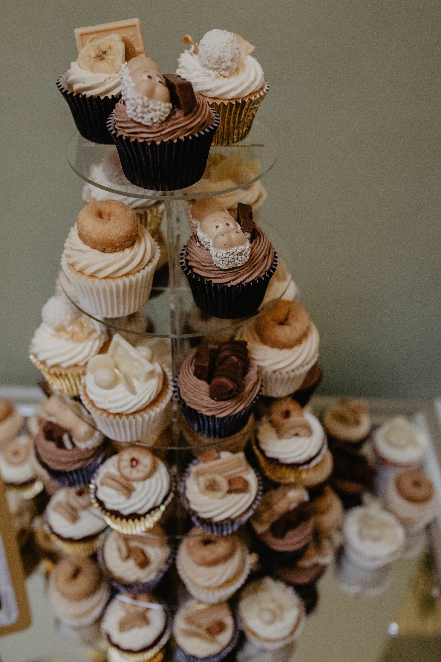 Cupcakes on a tiered stand, varying frosting colors and toppings, displayed on a mirrored surface.