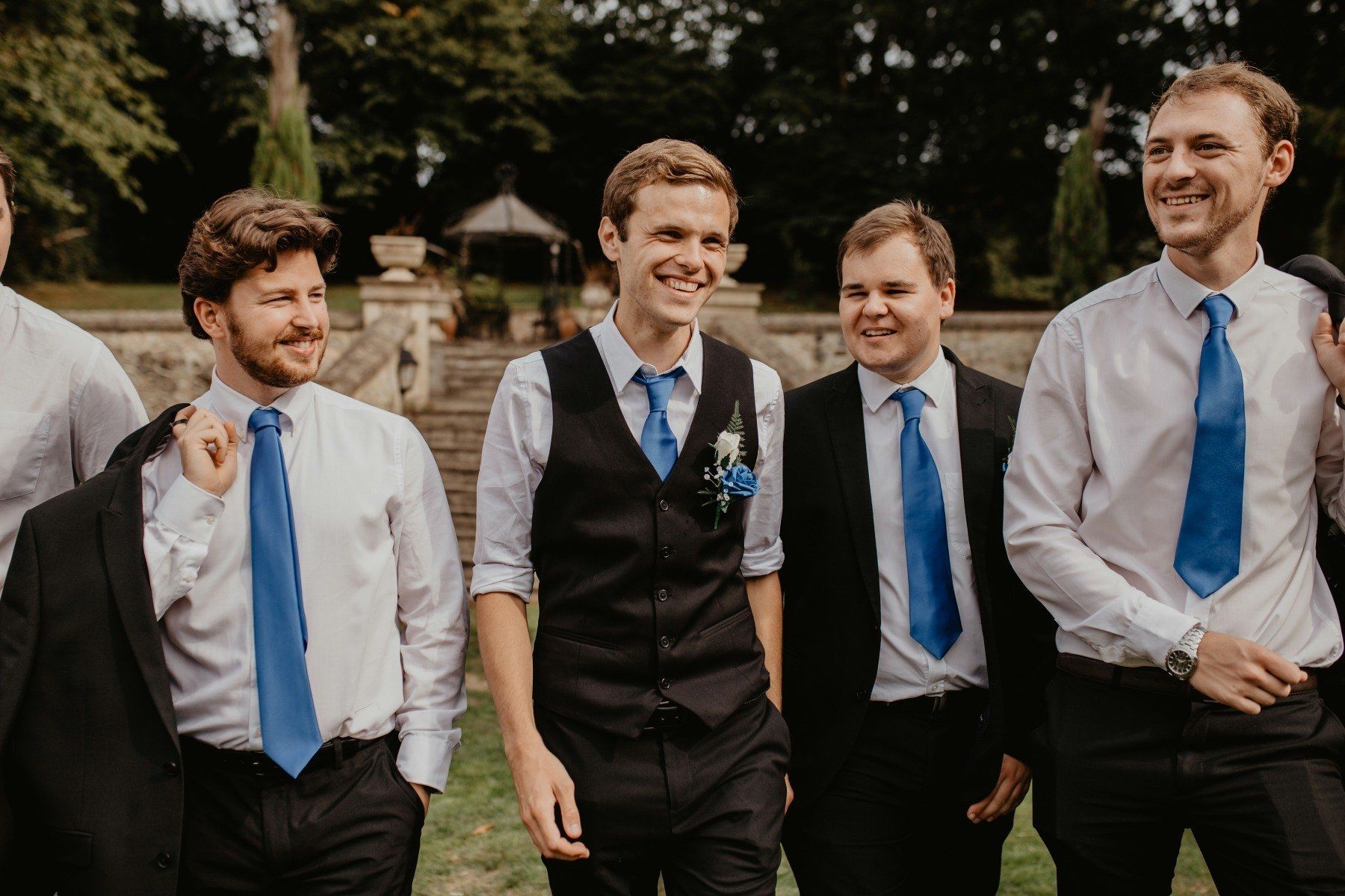 Five men in suits and ties, smiling, walking outside.