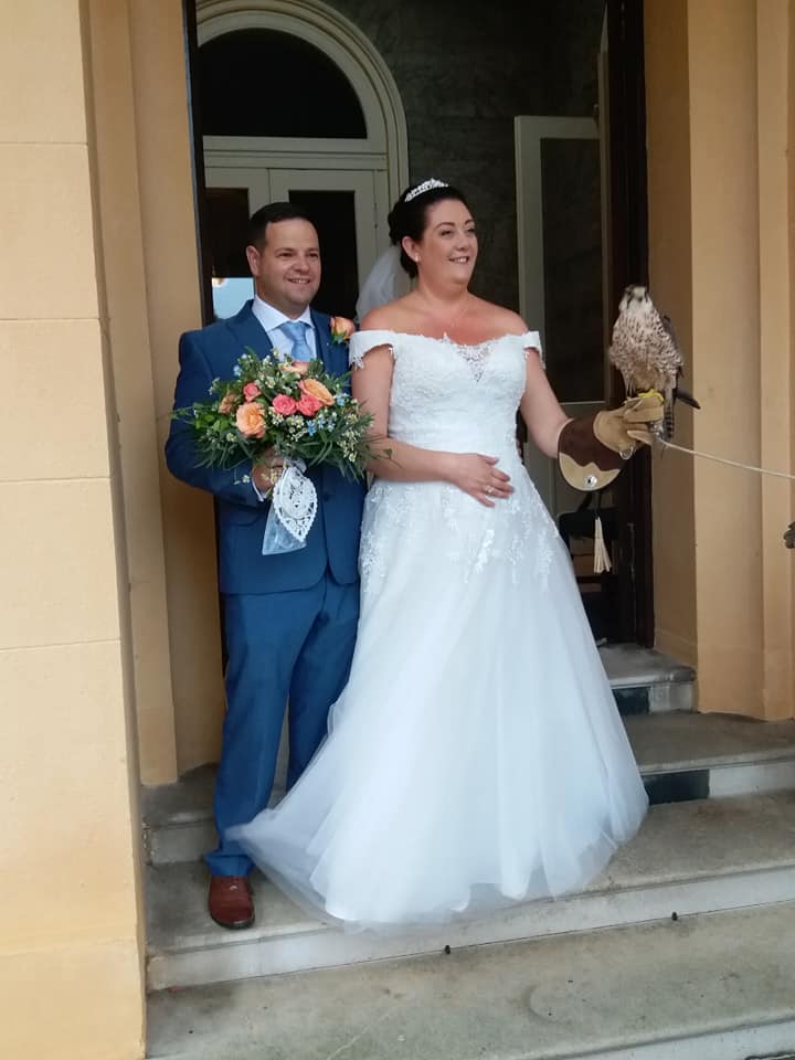Bride and groom pose on steps with a falcon; the bride holds a falcon on her arm, the groom has a bouquet.