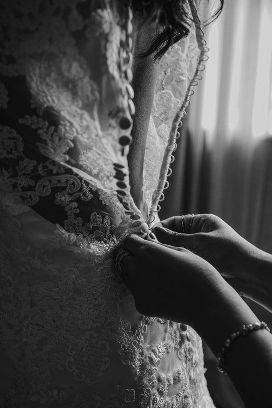 Woman's wedding dress being buttoned up by someone's hands. Black and white. Lace detail.