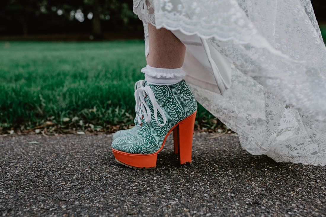 Bride's teal and orange platform booties with white lace and ruffled socks, peeking from under her wedding dress.