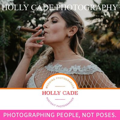 Advertise with Wight Wedding Days Bride exhales cigar smoke. Wearing a white dress with netting over shoulders. Outdoor setting. Photographer's logo and text.