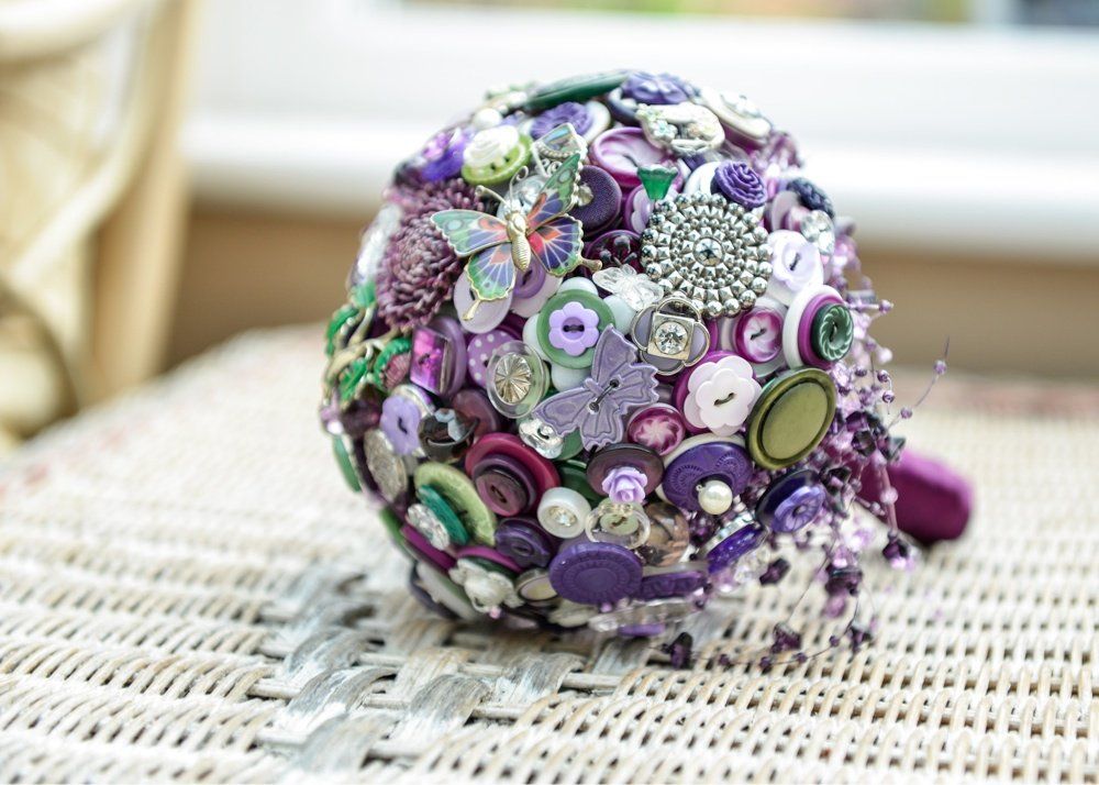 Button bouquet, primarily purple, on a wicker surface; details include a butterfly and beads.