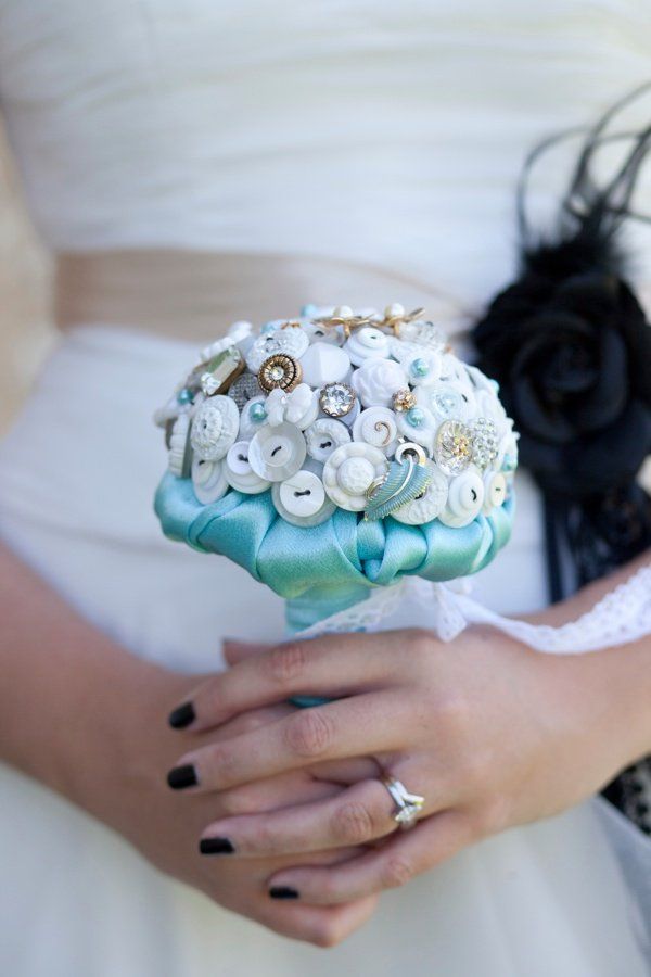 Bride holding a button bouquet, wearing a white dress and black nail polish.