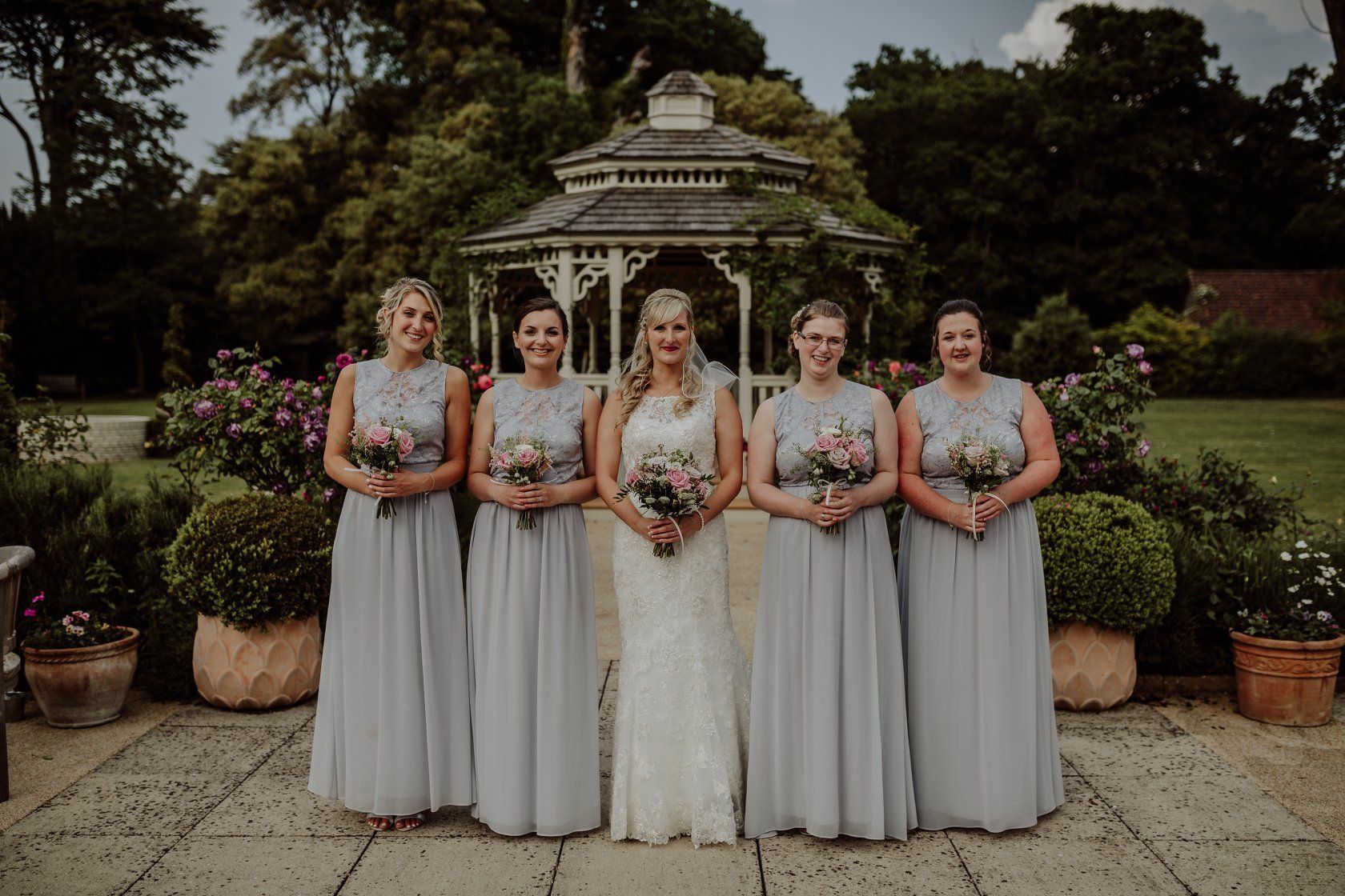 Bride with bridesmaids holding bouquets in garden.