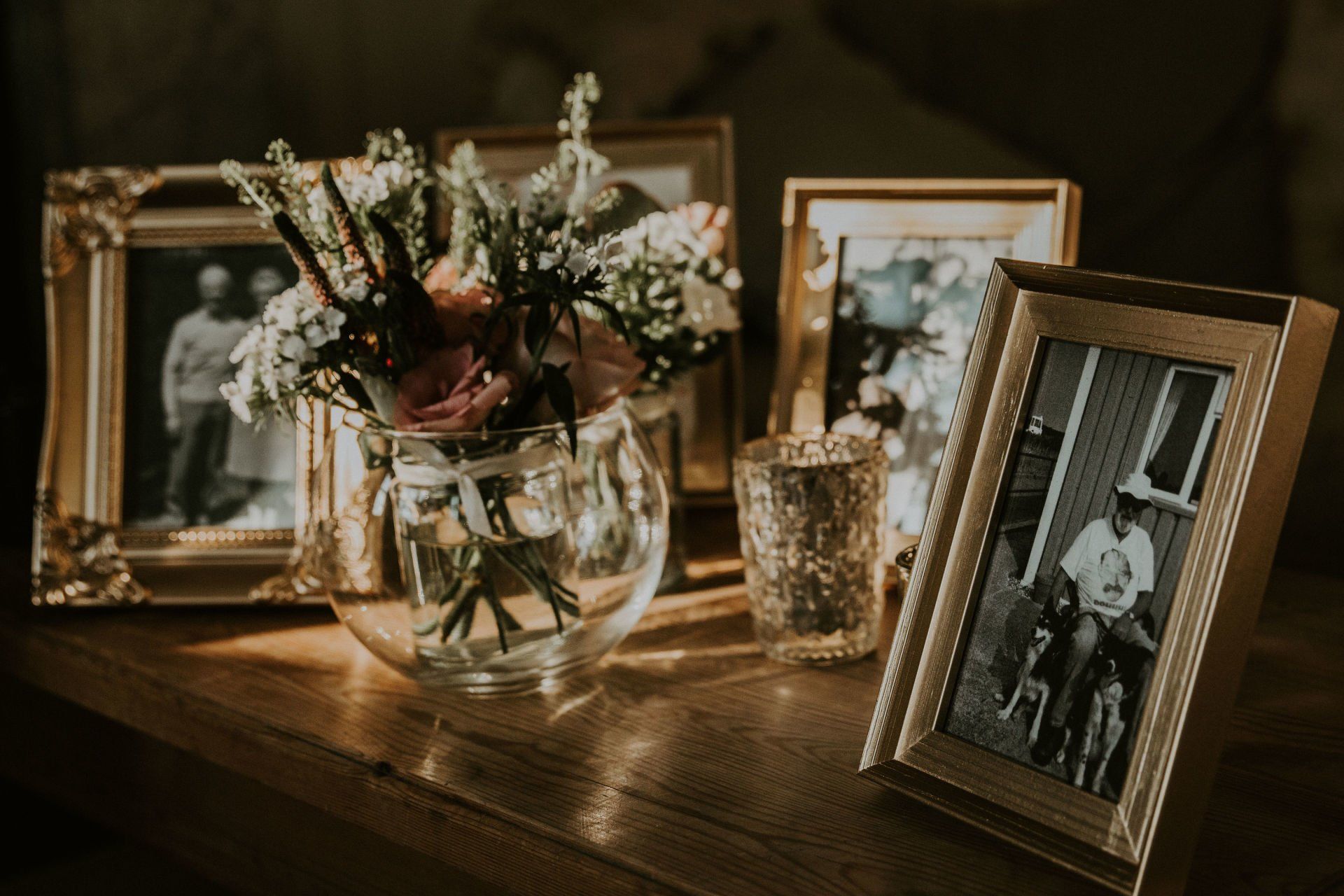Gold-framed photos and a flower arrangement on a wooden table, warm lighting.