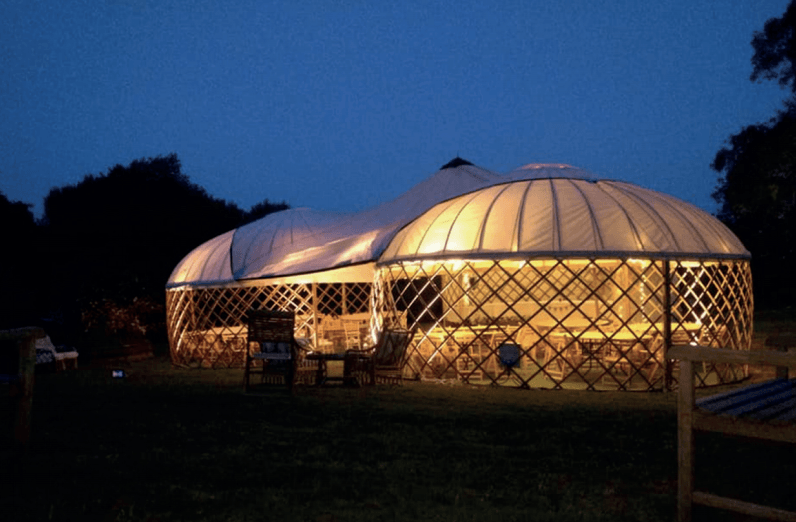 Lit yurt-style structure at dusk with a round top and open lattice walls.