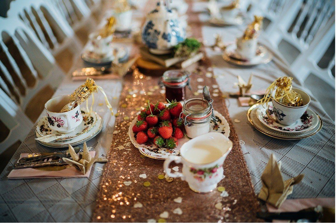 Table set for tea: strawberries, cream, jam, and floral china on a glittery runner.