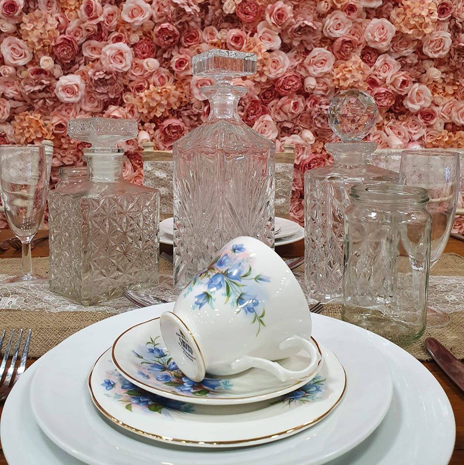 Teacup on a set table with crystal decanters and a rose flower wall backdrop.