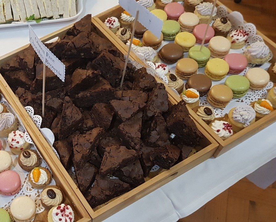 Wooden trays filled with brownies, macarons, and mini cupcakes on a table.