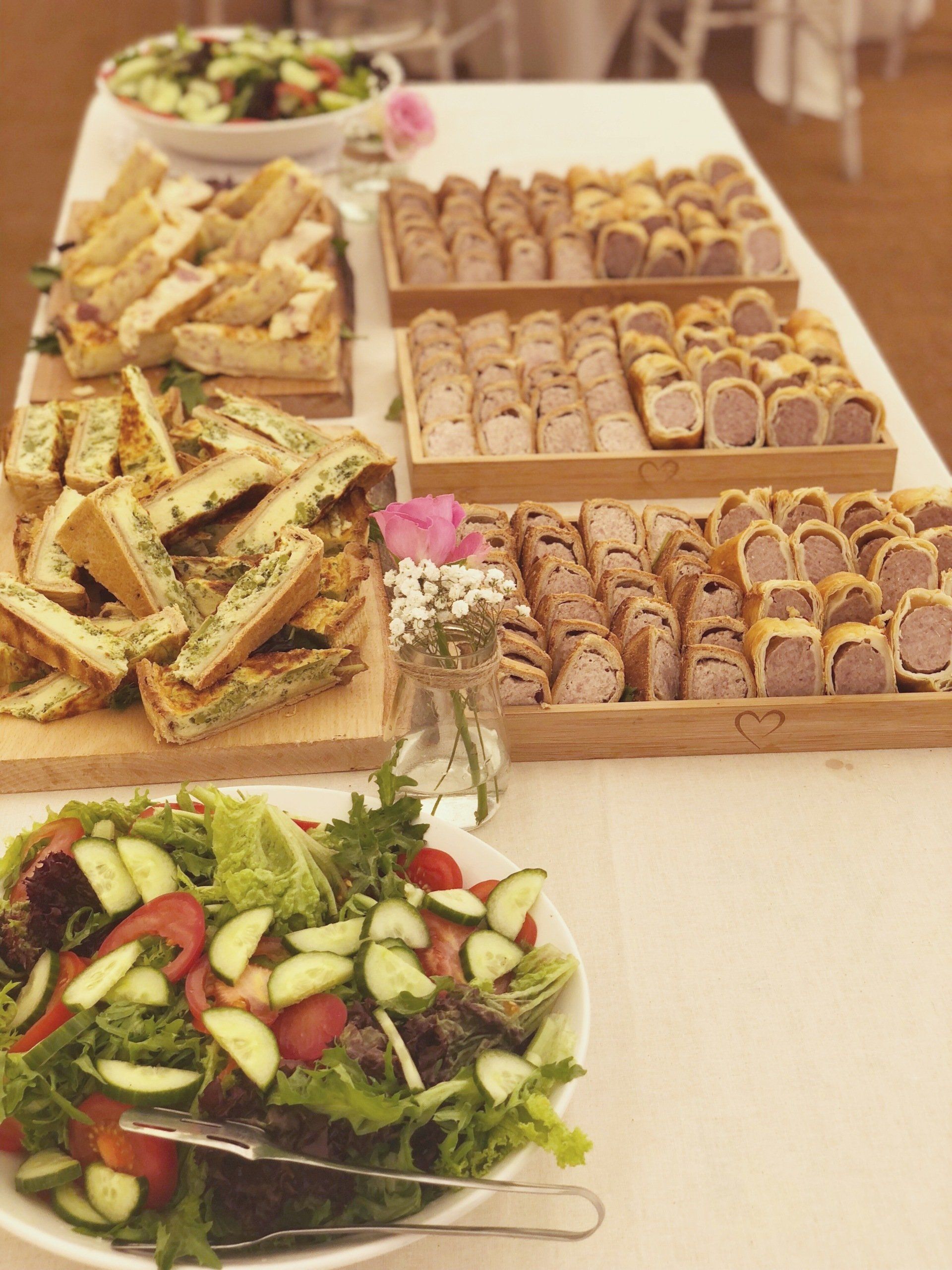 Buffet table with assorted sandwiches, sausage rolls, and salads.