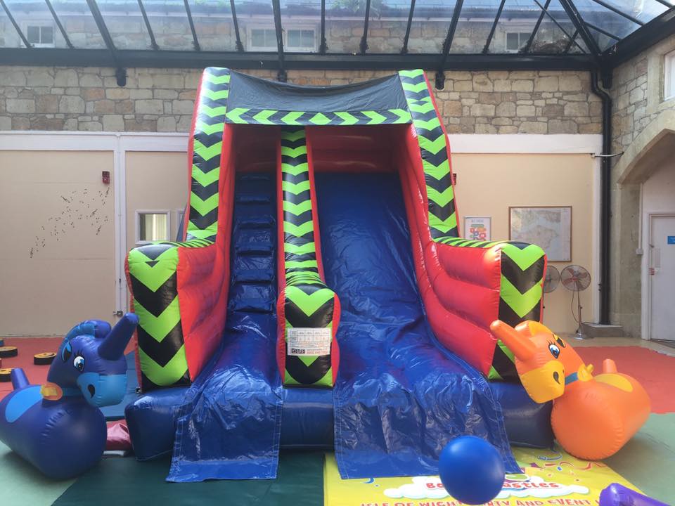 Inflatable water slide with red, black, green, and blue colors, with animal-shaped bouncy toys nearby.