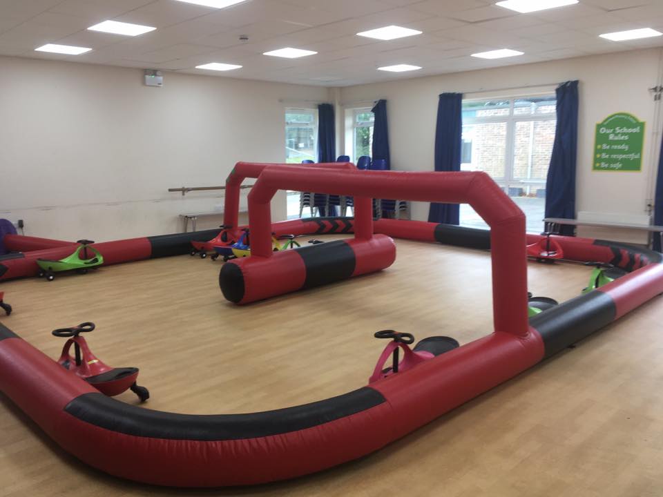 Indoor inflatable race track with red and black barriers. Toy cars are on the track.