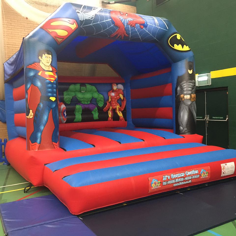 Superhero-themed bouncy castle with Superman, Hulk, Iron Man, and Batman graphics, red, blue, and black colors, indoor setting.