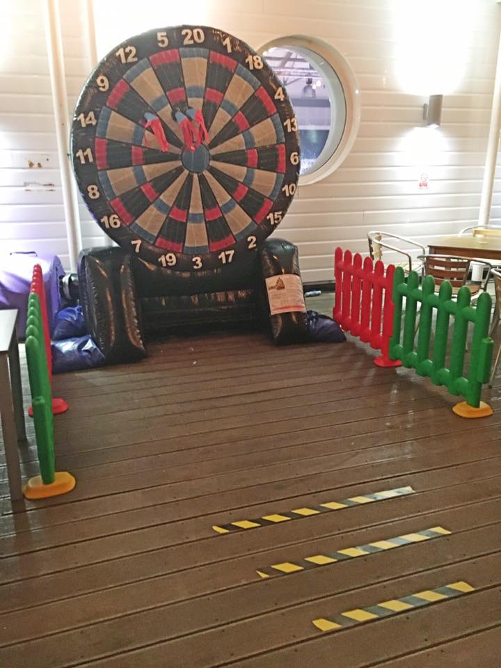 Dartboard game set up indoors with red and green barriers and distance markers.
