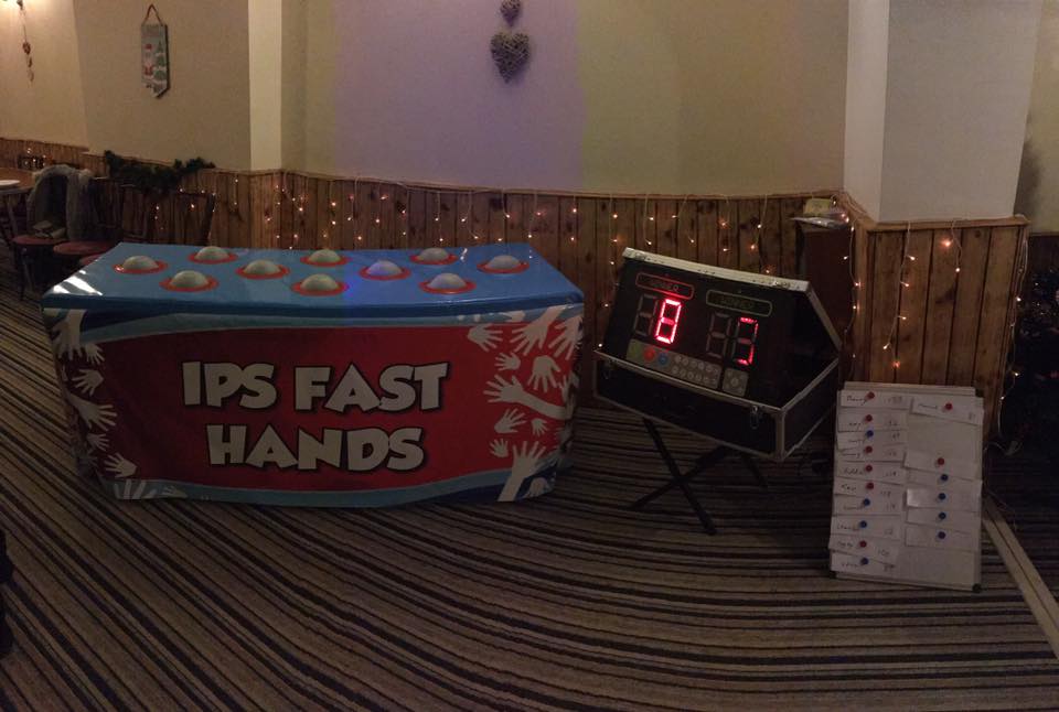 IPS Fast Hands game: a red and blue box with glowing lights, a digital scoreboard, and control panel, indoors.