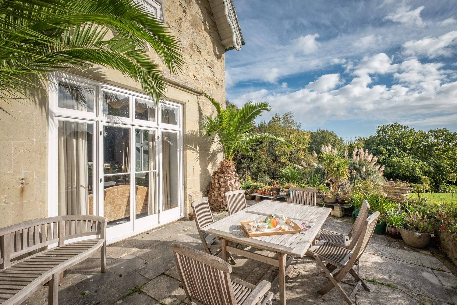 Patio with wooden furniture, palm tree, and garden view on a sunny day.