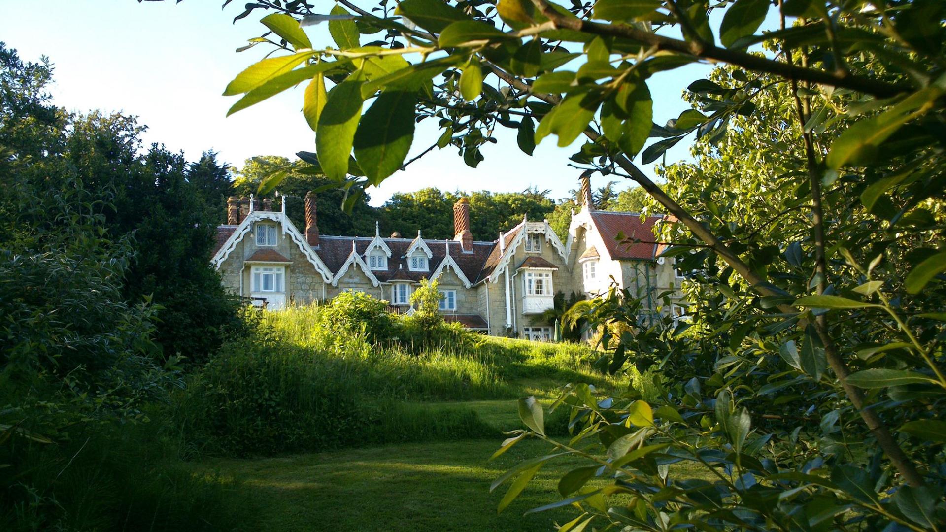 A stone house with multiple dormers, nestled among lush greenery under a sunny sky.