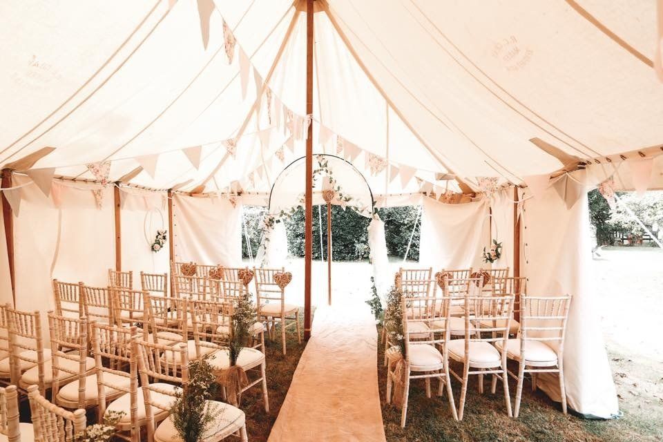 Wedding tent interior with rows of chairs, a central aisle, and decorations; soft colors.