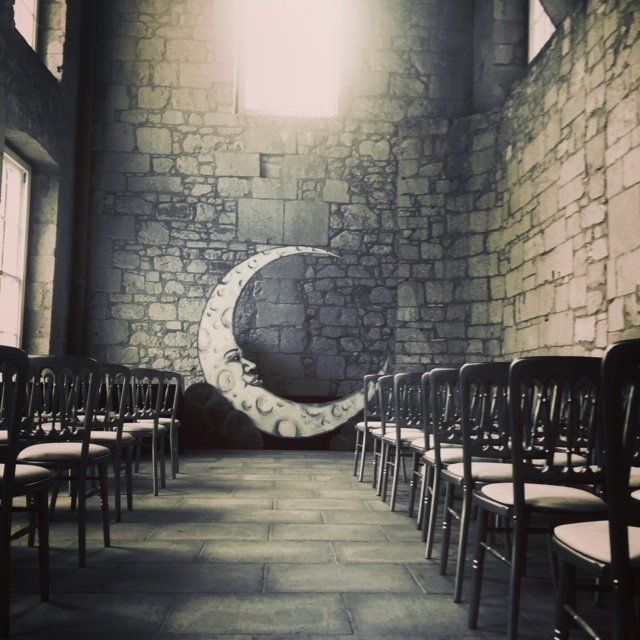 Rows of chairs face a stone wall with a crescent moon painted on it in a dimly lit room.