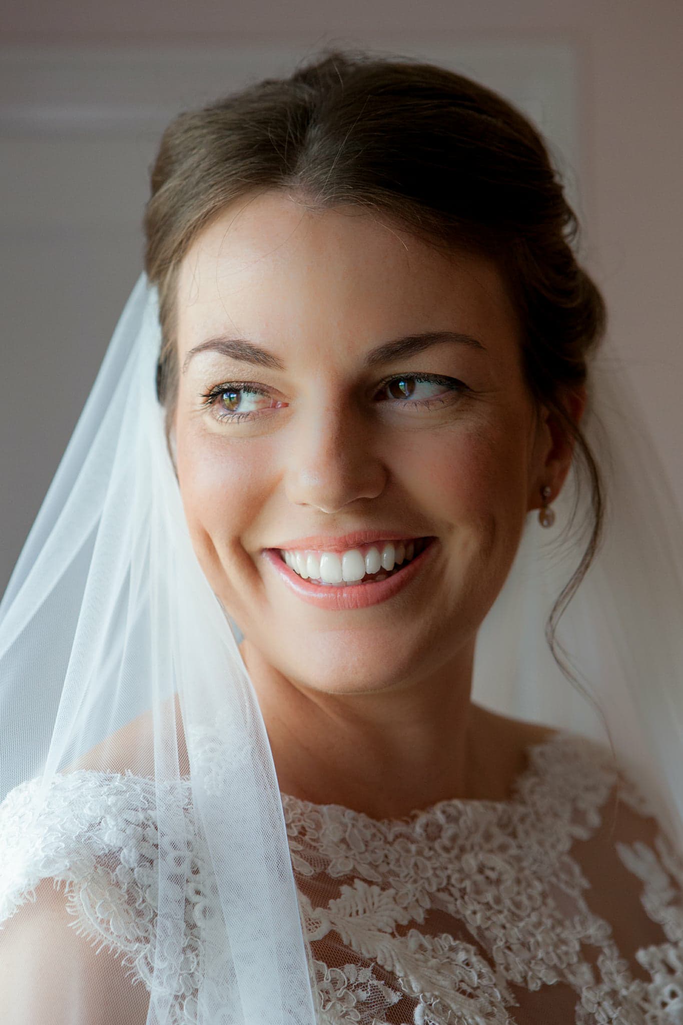 Woman smiling in wedding dress, veil, and updo hairstyle.