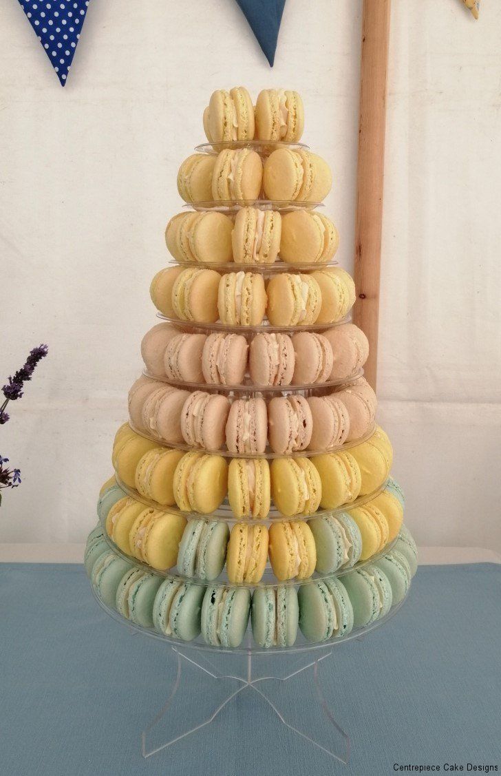 Macaron tower with pastel-colored treats. It is stacked on a clear stand, on a blue tablecloth.