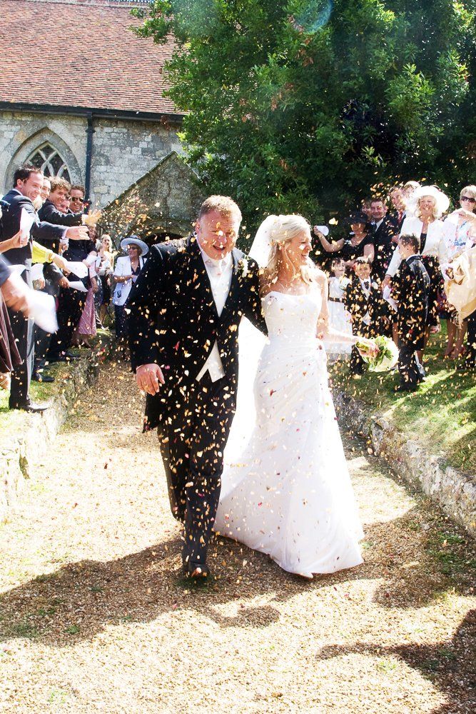 Newlyweds walk out of a church, covered in confetti.