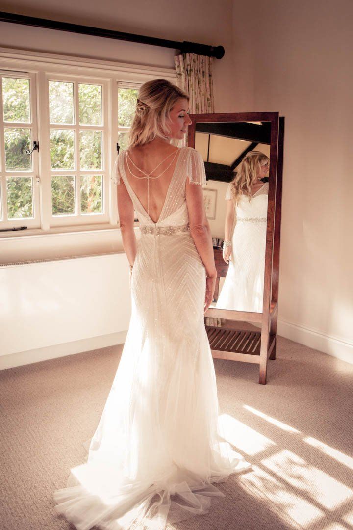 Woman in wedding dress looking in mirror in sunlit room.