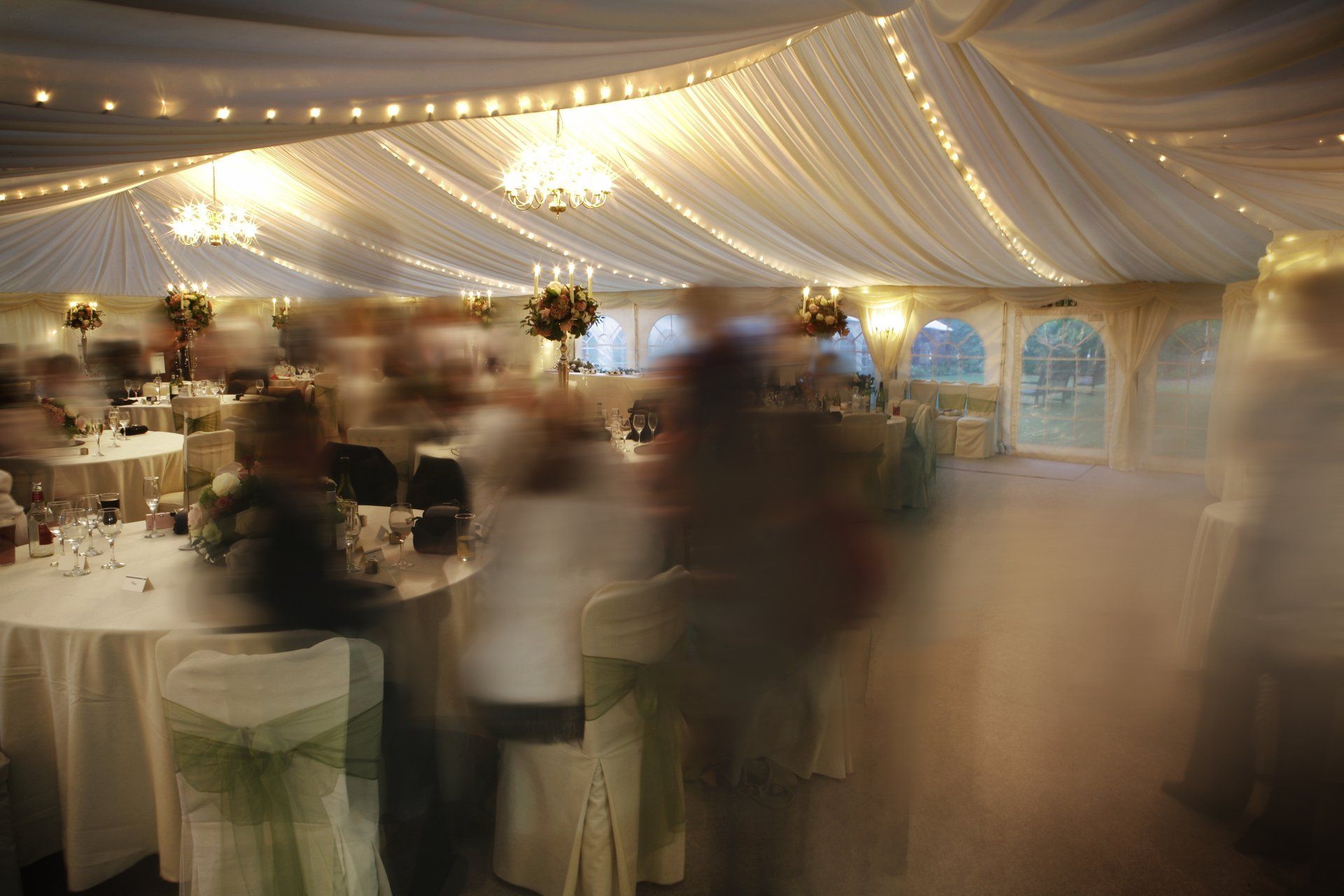 Marquee interior, blurry people milling about tables, string lights and chandeliers.