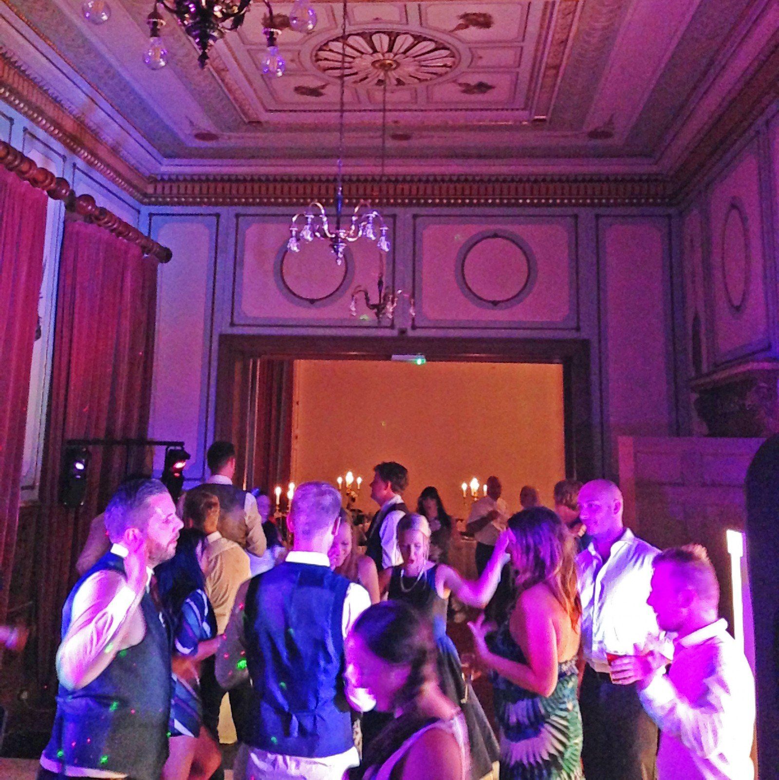 People dancing in a room with ornate ceiling and walls, lit with colorful lights.