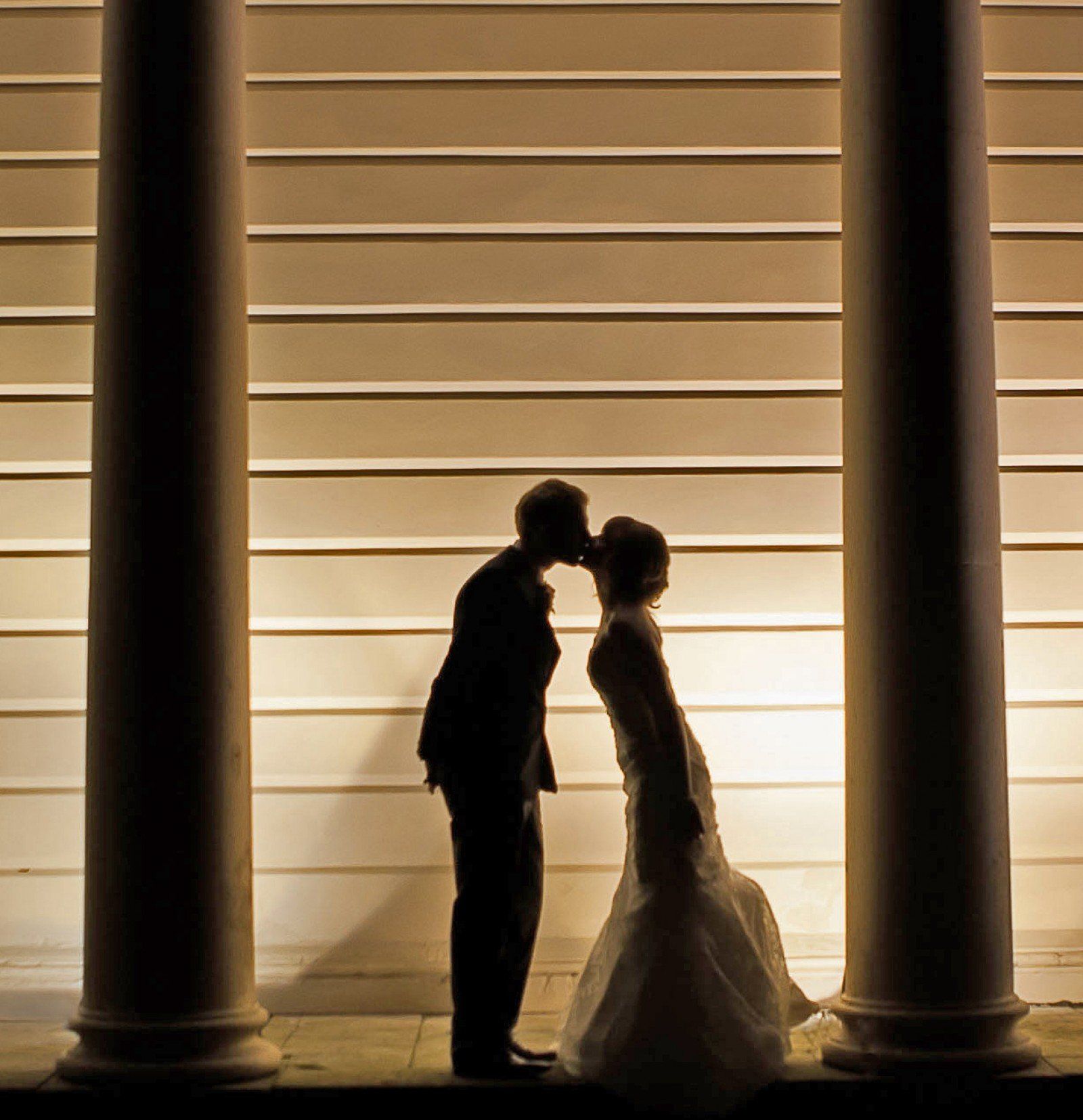 Silhouette of a kissing couple on their wedding day; columns frame them against a horizontally striped wall.